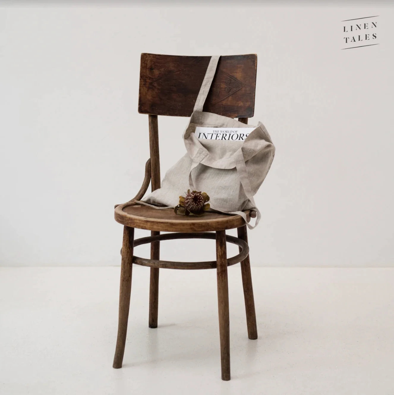 En tote bag i naturell linnetyg med långa handtag som står på en stol.