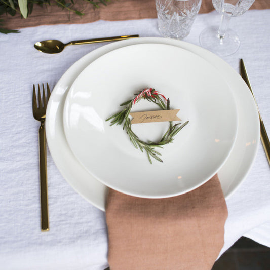 En aprikos färgad linneservett ligger mellan två vita tallrikar på ett dukat bord.