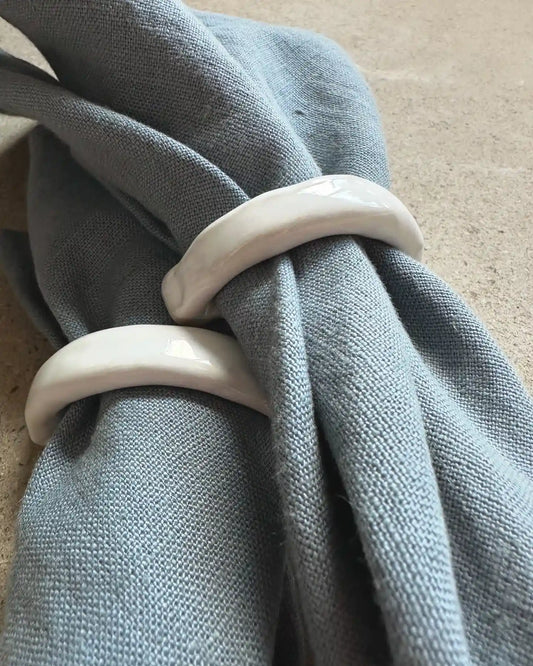 Två vita servettringar i glansig keramik med blå linneservetter