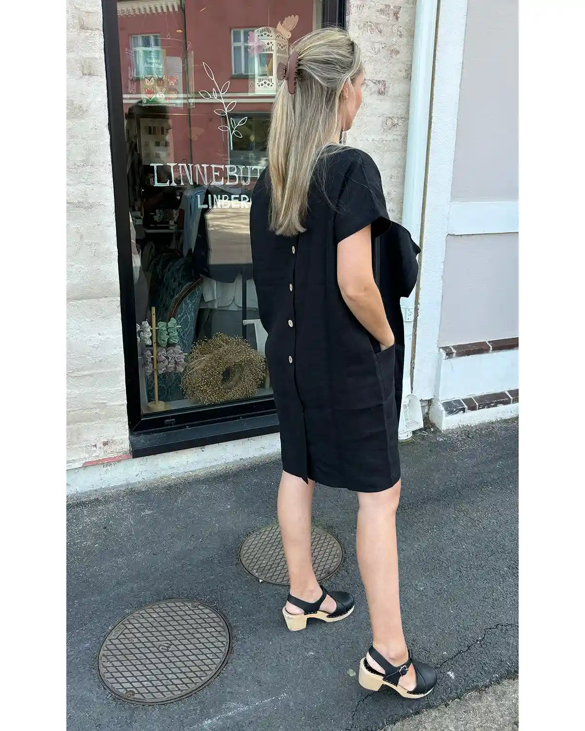Modellen bär en svart-shirt klänning med träknappar i ryggen.