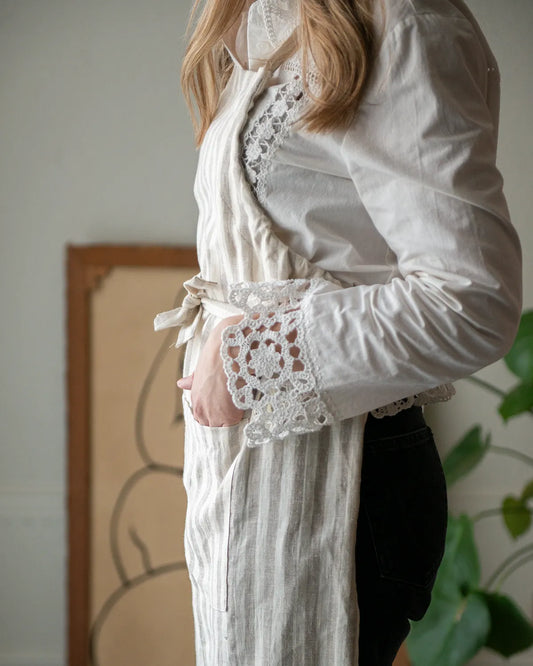 En kvinna har på sig en vit spetsblus och ett linneförkläde