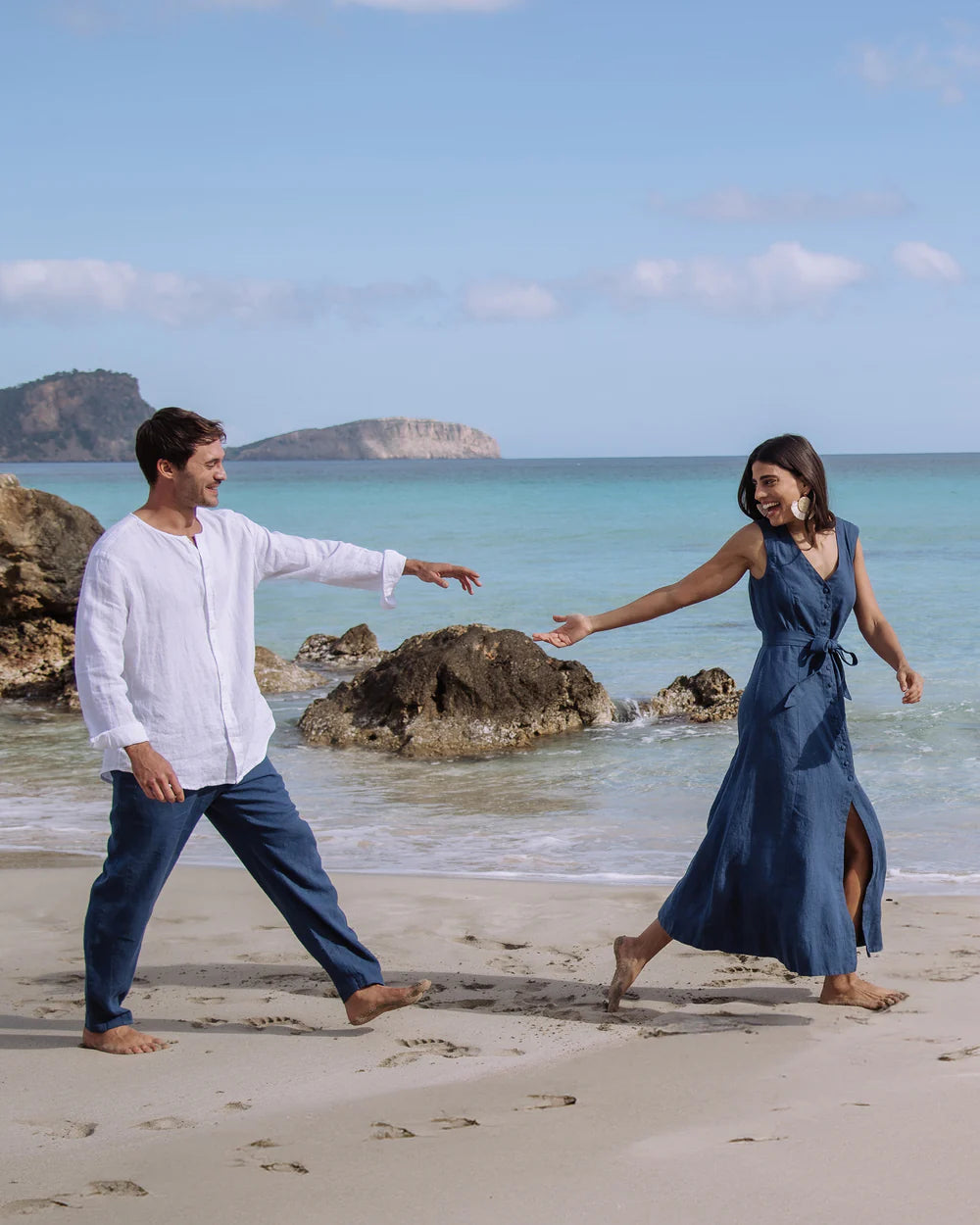 En kvinna har på sig en marinblå linneklänning och mannen har på sig marinblå linnebyxor