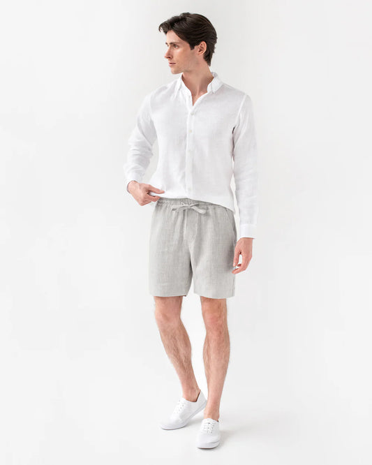 Mannen bär grå linneshorts och vit linneskjorta.