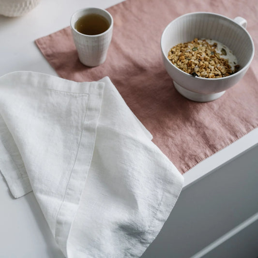 En dukning med en aprikos bordstablett och vit linneservett som ligger slarvigt placerad på frukostbordet.