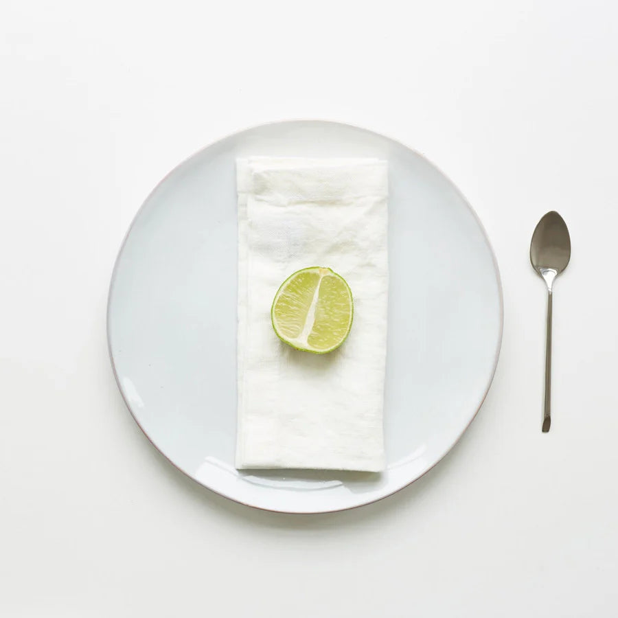 En vikt, vit tygservett på en vit tallrik med en halvt skivad lime på toppen.