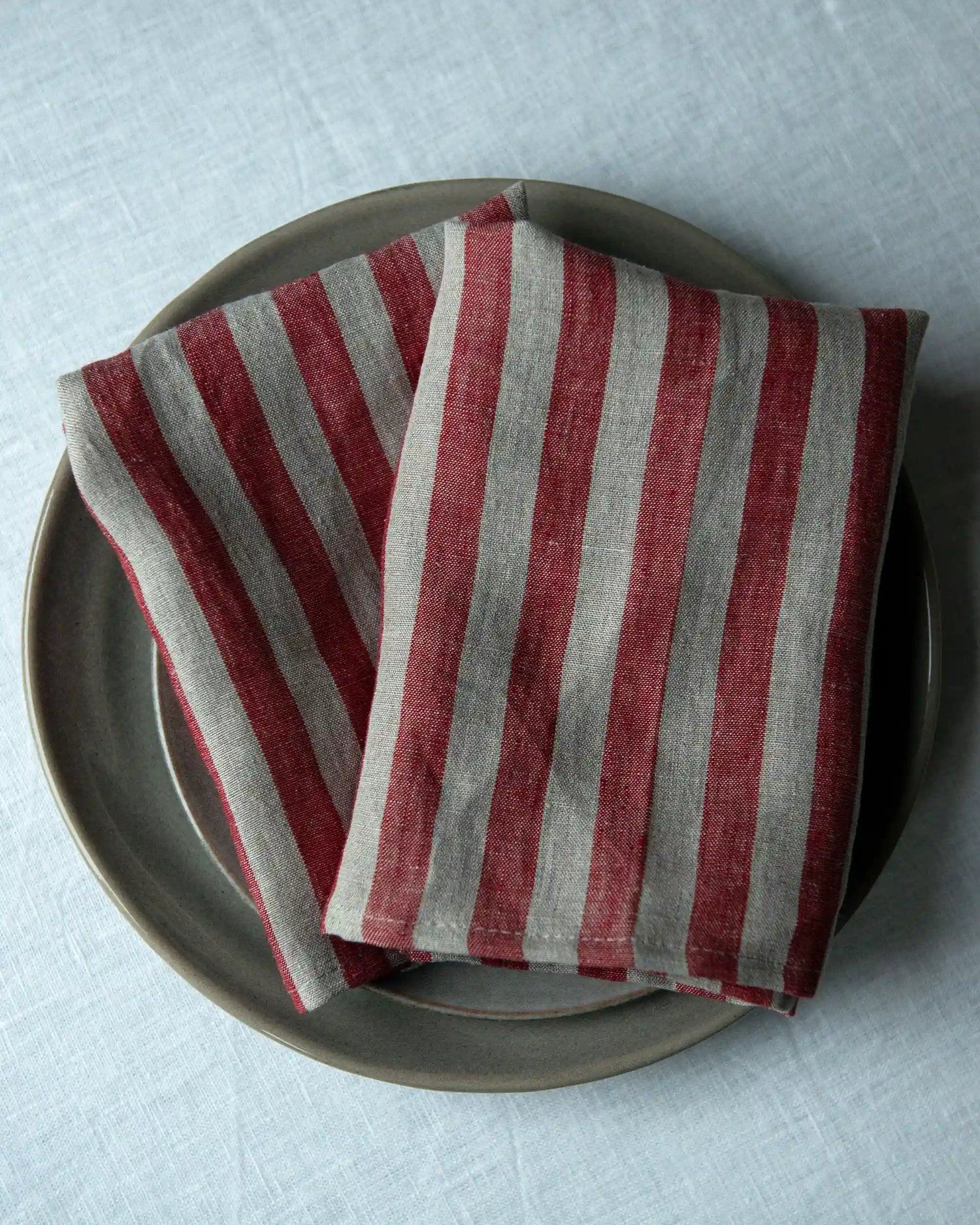 Två stycken handsydda linneservetter med röd och beiga ränder ligger vikta på en tallrik. 