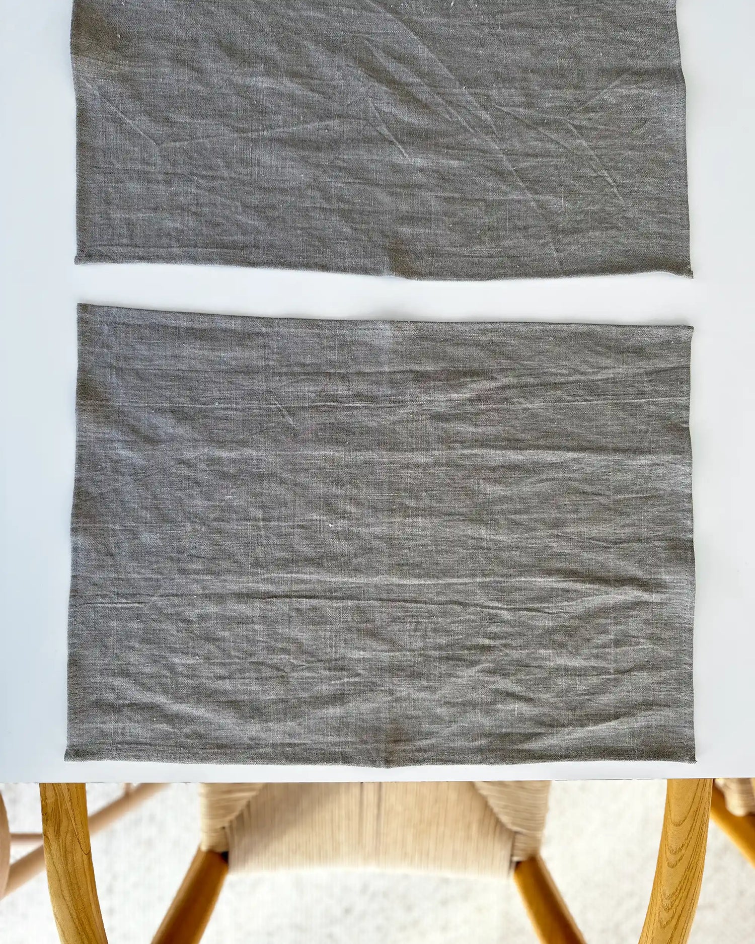 Två handsydda bordsunderlägg i stentvättat linne som ligger dukat på ett vitt bord. 