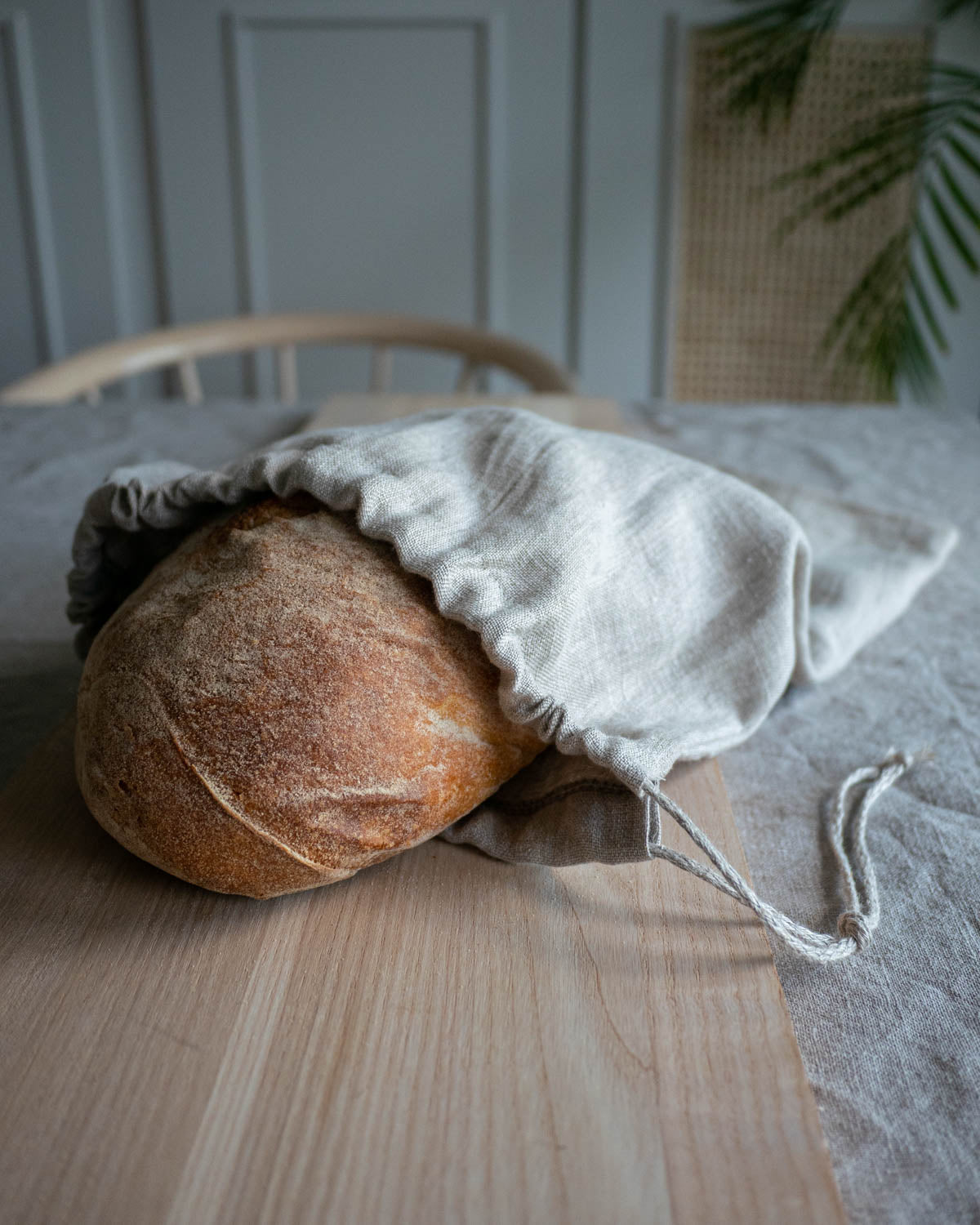 Brödpåse i naturell linnetyg som ligger på ett träbord. I brödpåsen ligger ett surdegsbröd som skymtar i öppningen. 