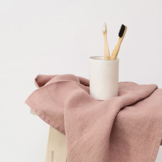 Liten våfflad handduk i aprikosfärg som ligger över en träbänk. På den våfflade handduken står ett glas med tandborstar.