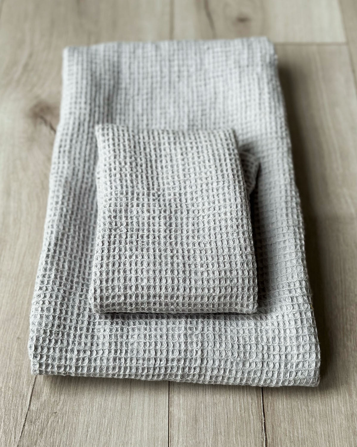Två beige våfflade linnehanddukar i olika storlekar ligger ihopvikta på varandra.