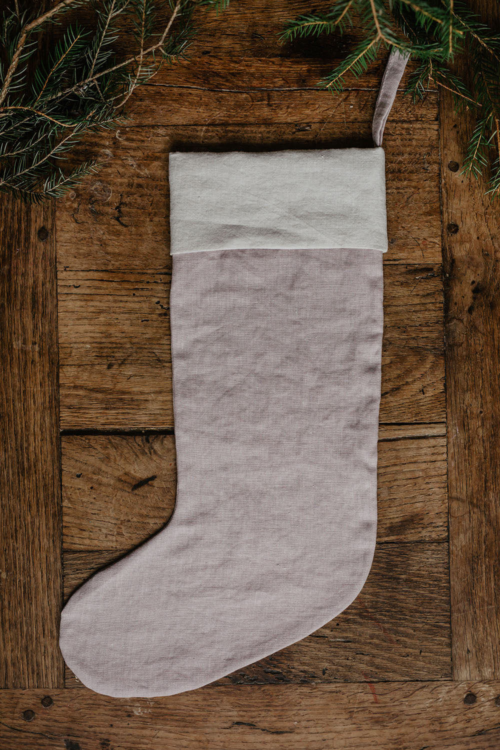 En ljusrosa julstrumpa i linne med en ögla ligger på ett träbord.