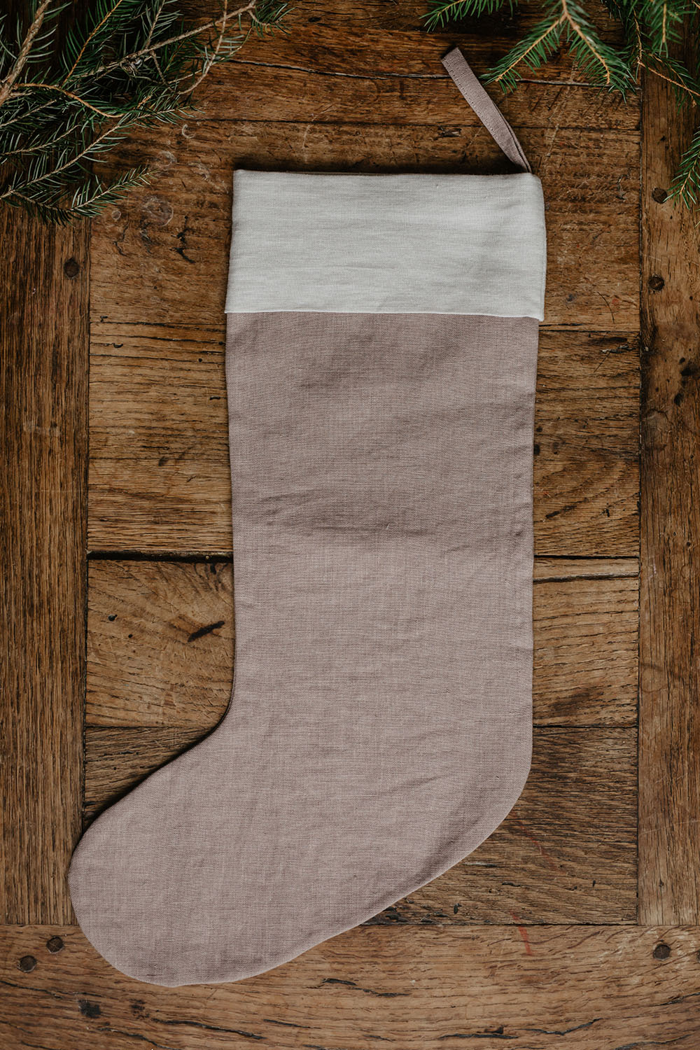 En ljusbrun julstrumpa i linne och med ögla ligger på en träskiva.