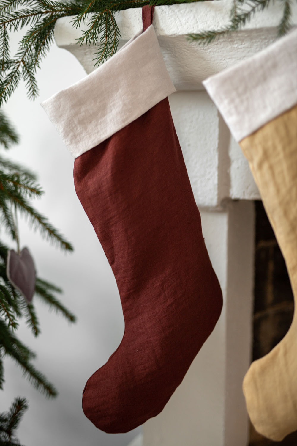 Två stycken julstrumpor i linne hänger upp sina öglor framför en öppen spis. 