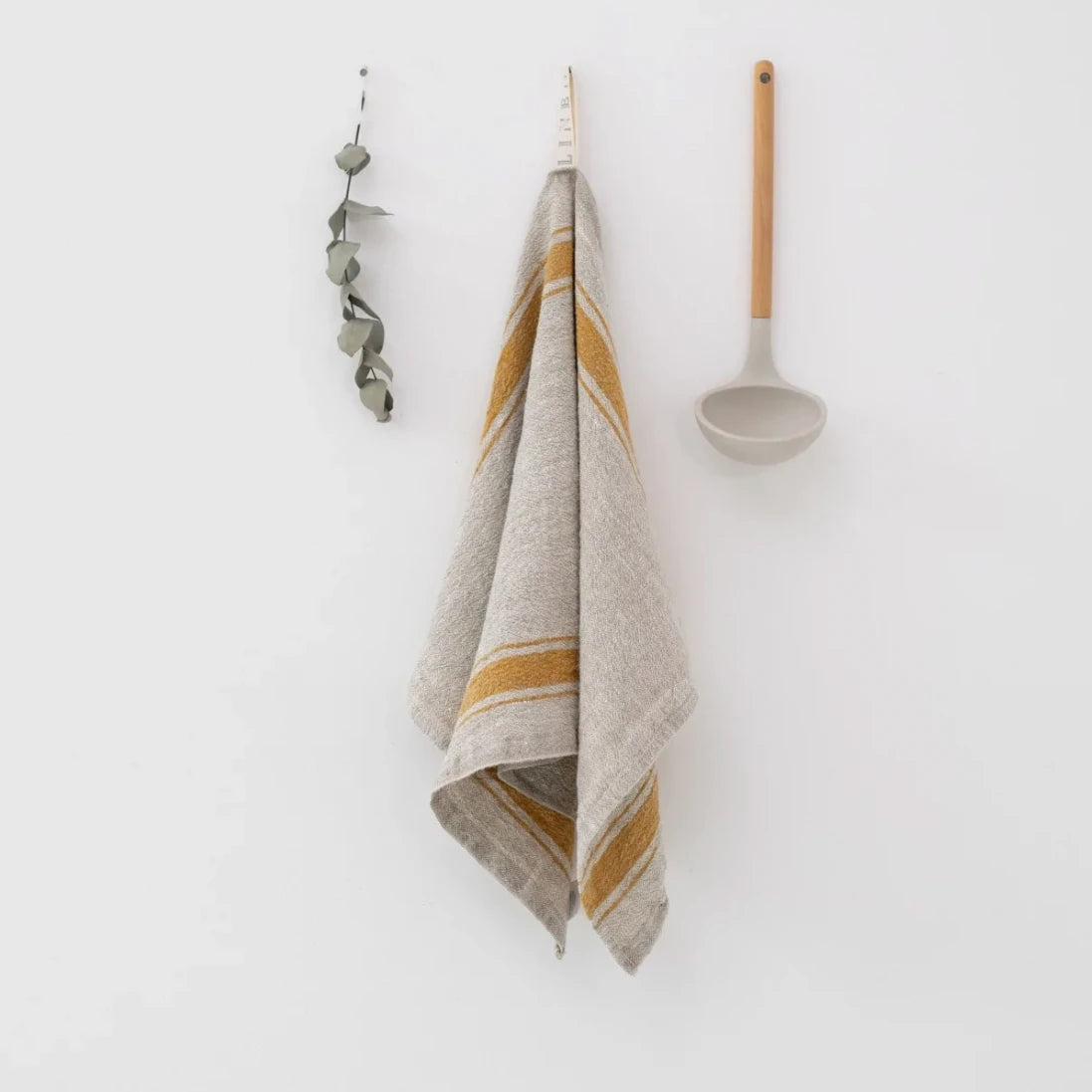 En handsydd naturell linnehandduk hänger i sin ögla på en kroklist.