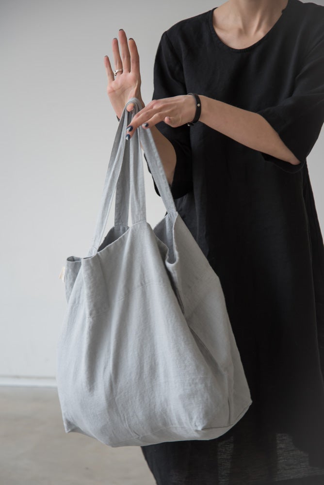 En kvinna håller fram en grå stor tygpåse i linne med medellånga handtag. 