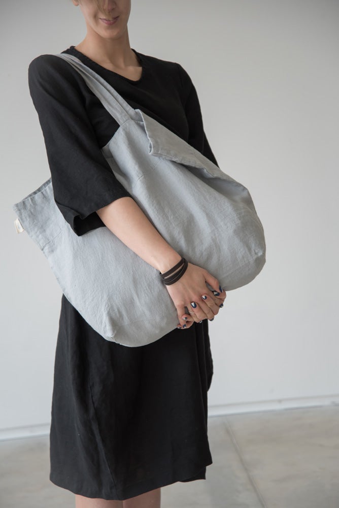 En kvinna bär en grå stor tygväska i linne över axeln. 
