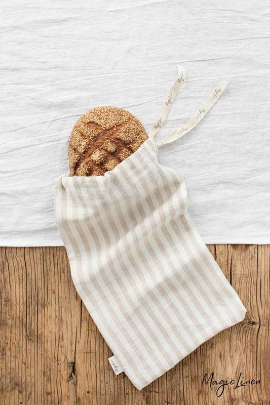 En rektangulär brödpåse i randigt linne som ligger på ett träbord med innehåll av bröd. 