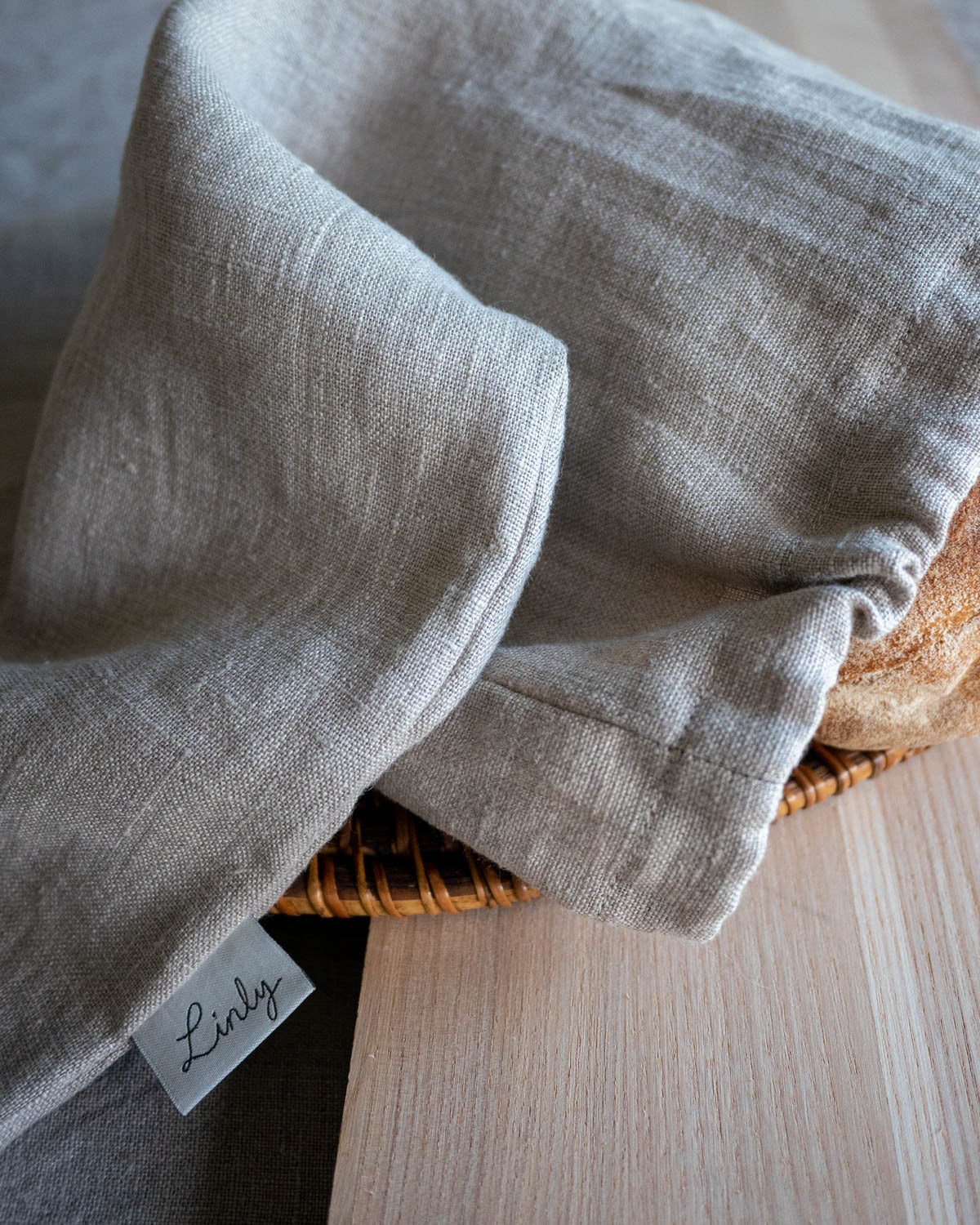Brödpåse i naturell linne som är vikt på mitten. Varumärkets namn är fastsytt på långsidan och där står det Linly. 