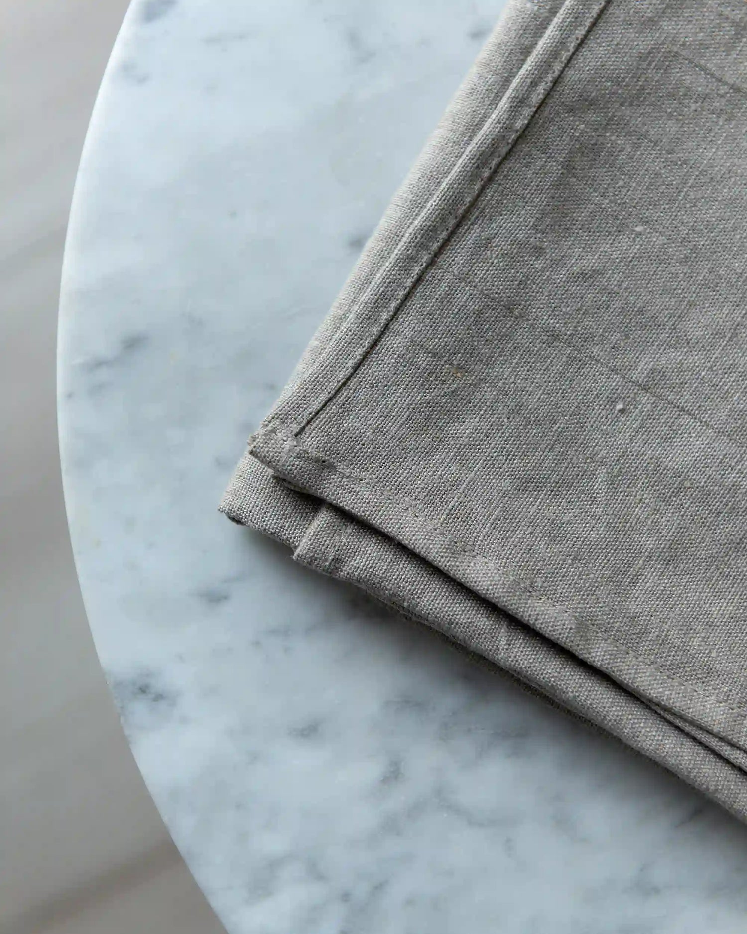 En naturell duk i linne ligger ihopvikt på en marmor yta. 