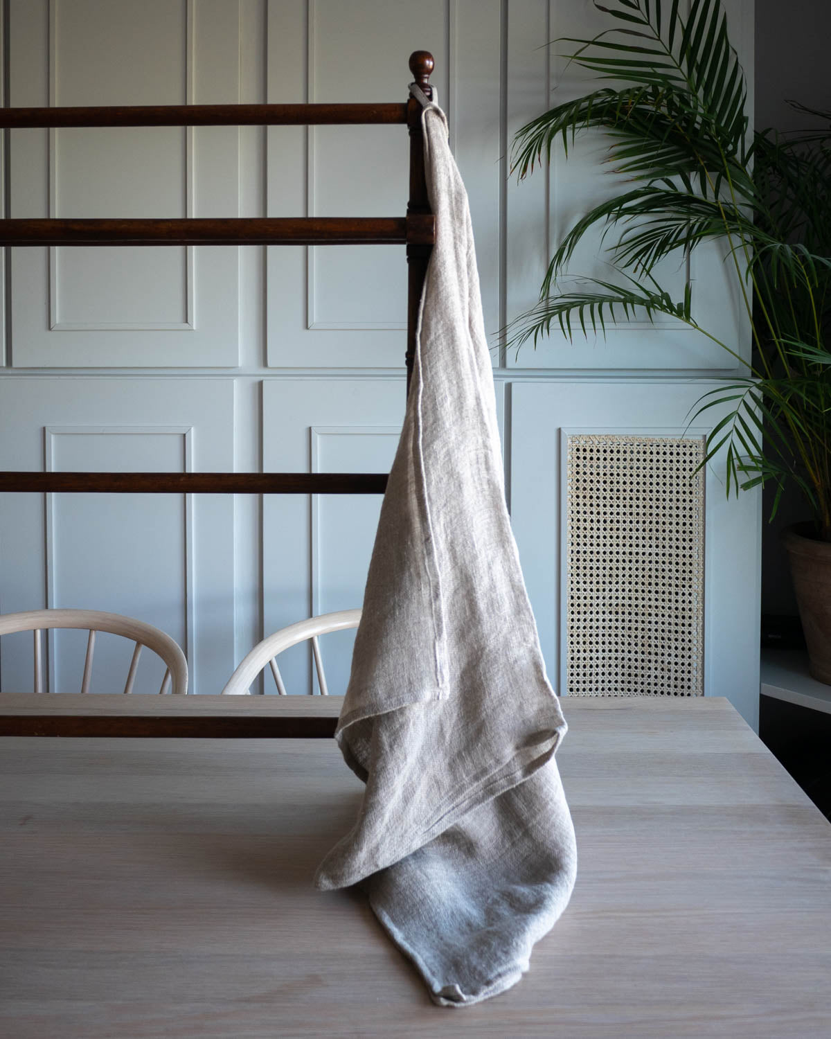 Medelstor handduk i naturell linne som hänger med sin ögla på en torkställning i trä. 