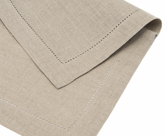 En beige linneservett med hålsöm ligger vikt på mitten.