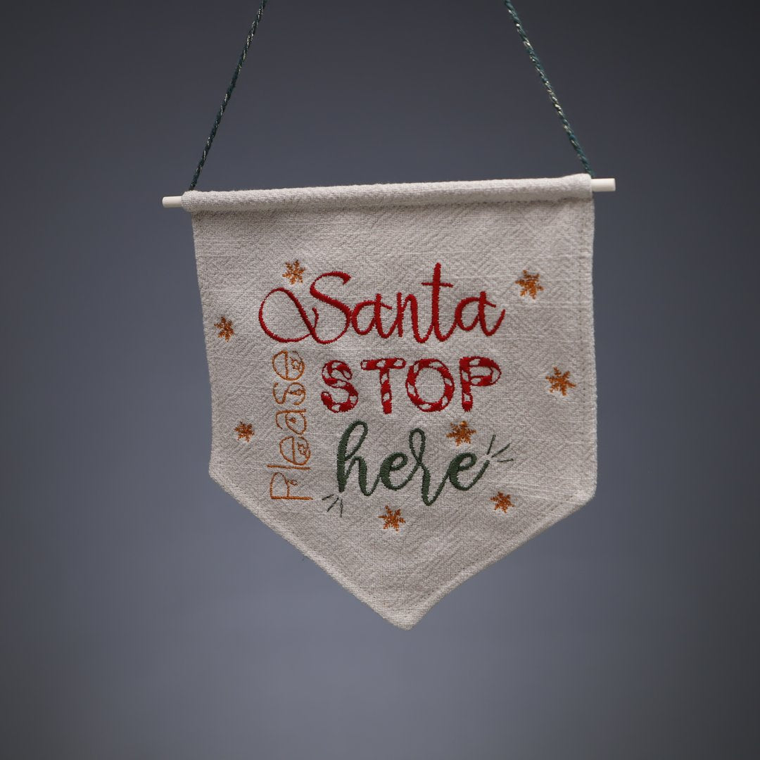 En liten vimpel i naturell linne med texten Santa please stop here.