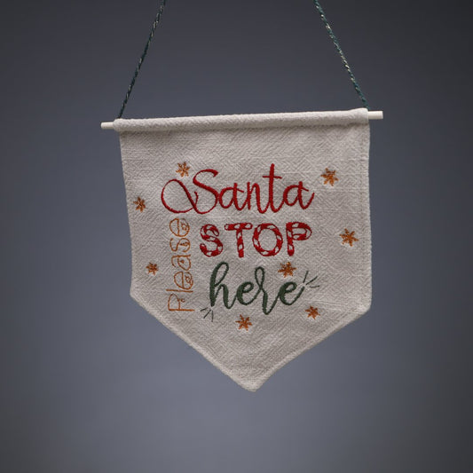 En liten vimpel i naturell linne med texten Santa please stop here. 