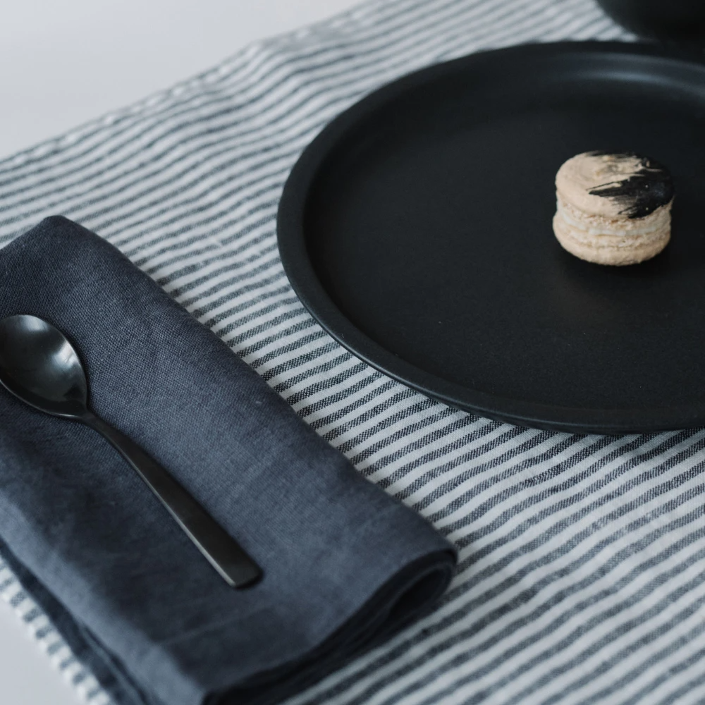 En handsydd mörkgrå linneservett som ligger vikt på en randig bordslöpare.