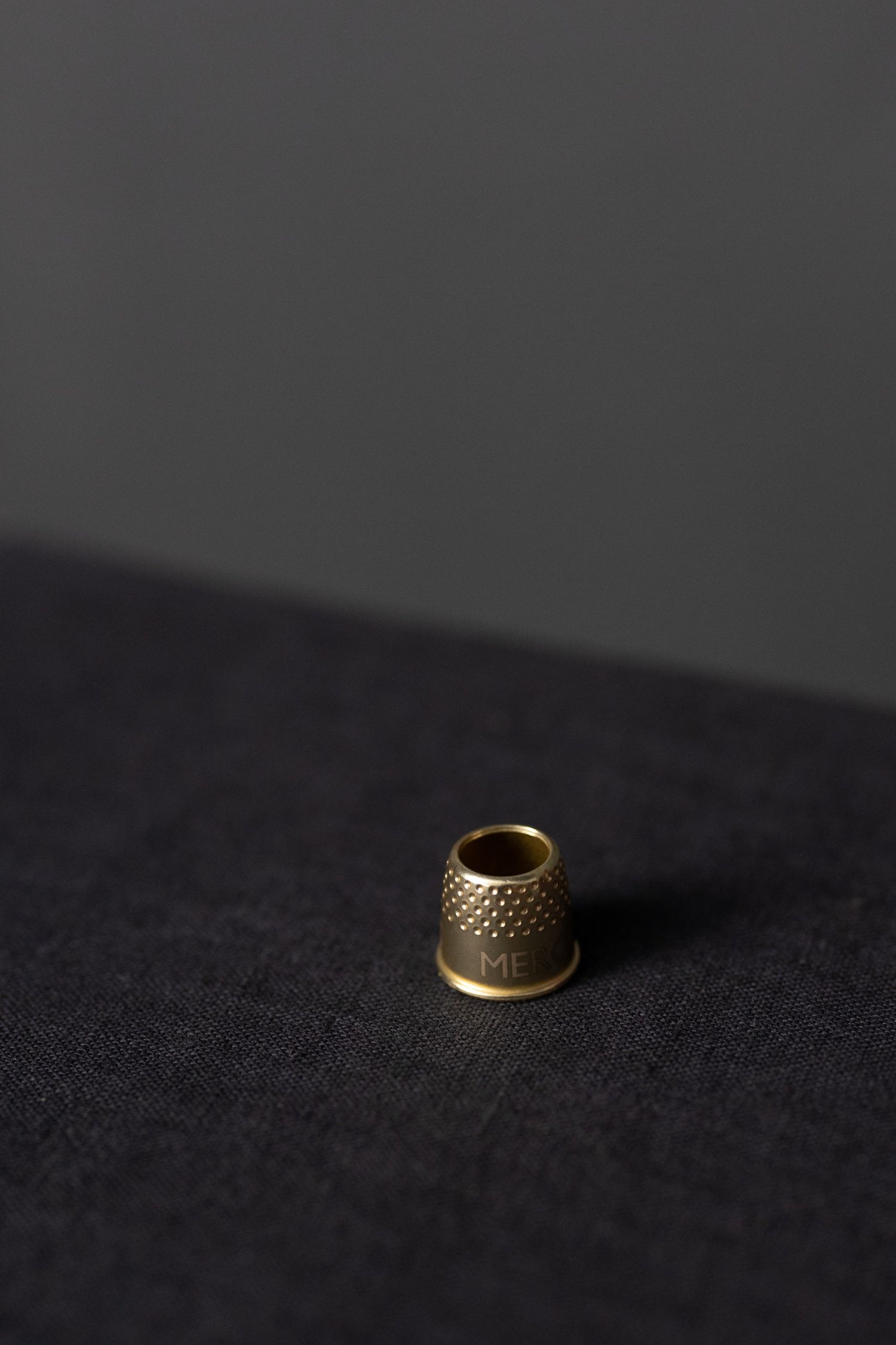 En liten fingerborg i mässing som står på en svart linneduk.