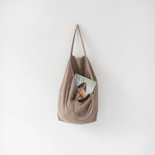 En handsydd tygväska i linne som hänger på en kroklist.