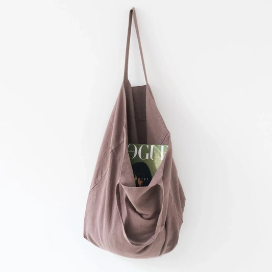 Medelstor tygväska i gammalrosa linne som hänger på en krok med sitt ena handtag. Väskan har formen av en rektangel med medellånga handtag. Från väskan skymtar en Vouge tidning.