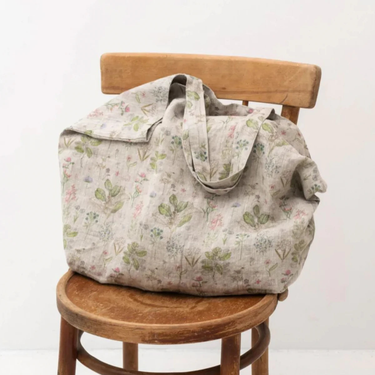 En stor tygväska i mönstrat linne med blommor står på en stol.