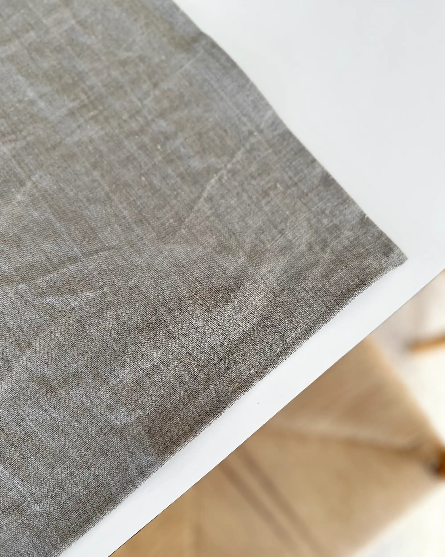Ett handsytt bordsunderlägg i stentvättat linne ligger på ett vitt bord. 