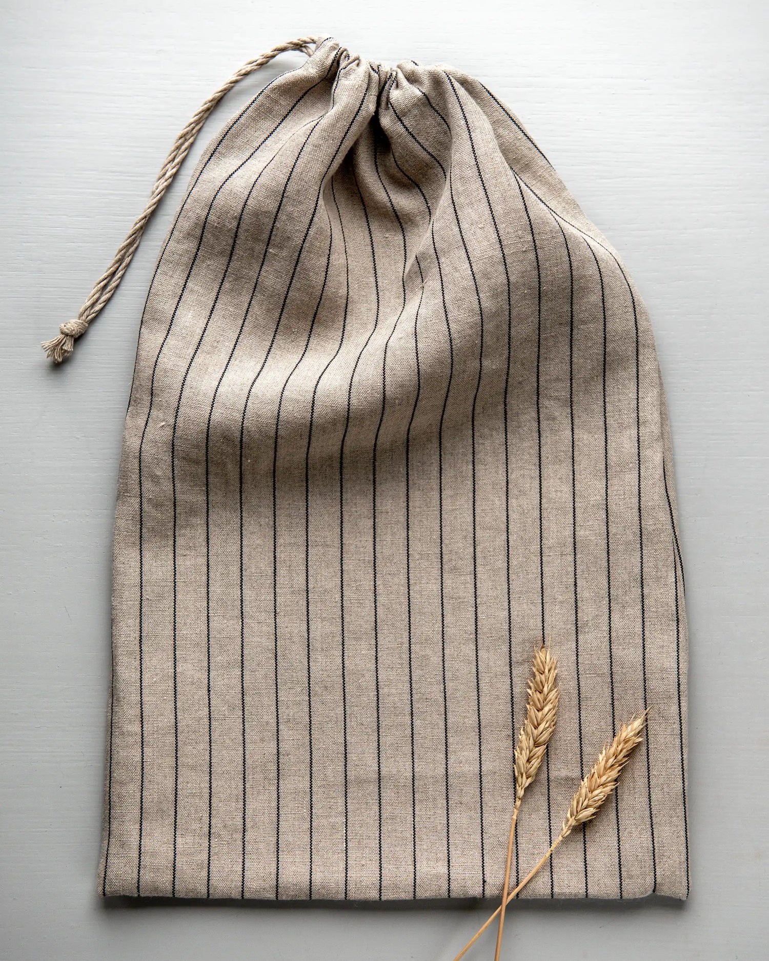En handsydd brödpåse i randigt linnetyg som har dragits ihop med ett tunt band. 