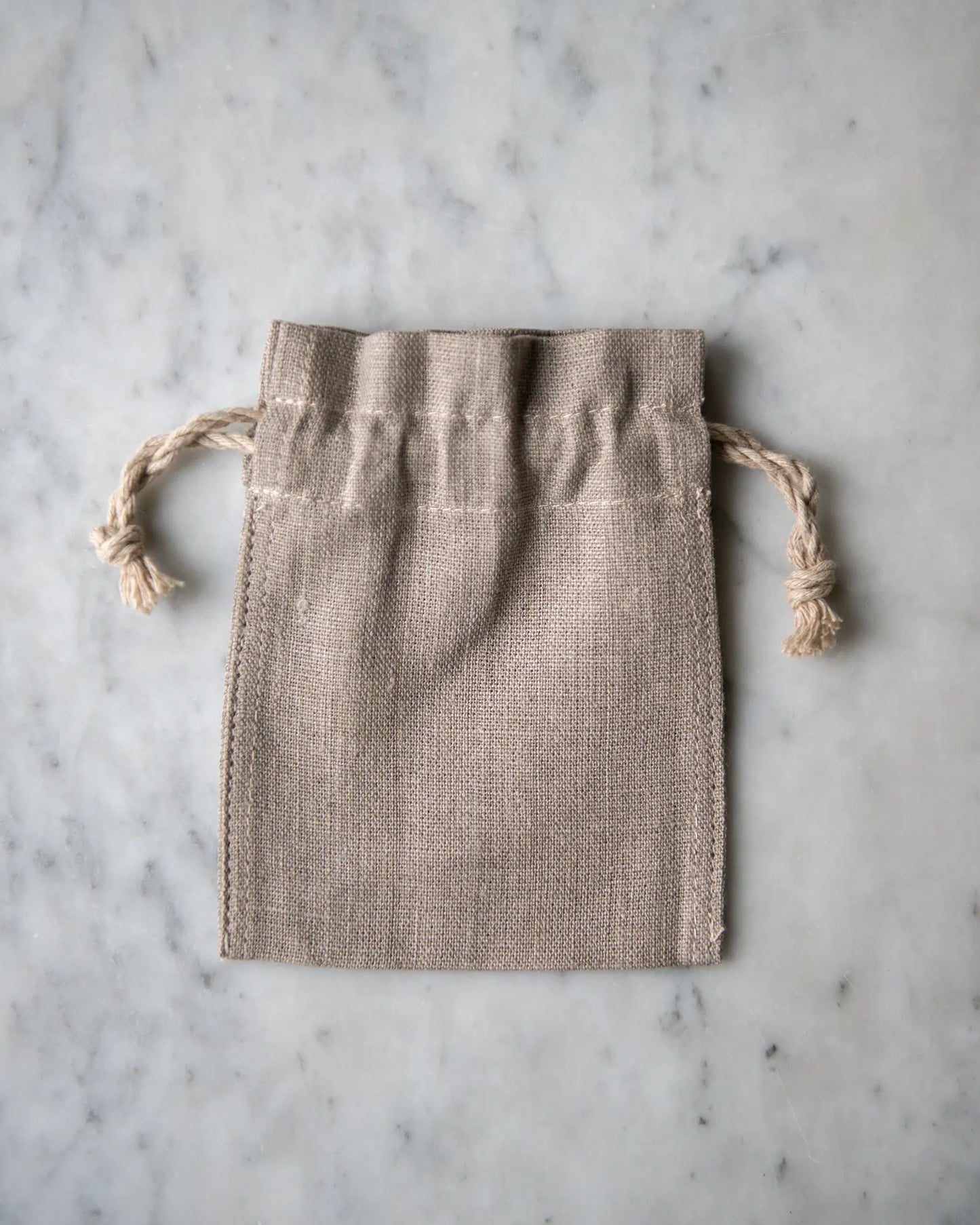 En liten handsydd linnepåse i beige ligger på en marmorskiva.