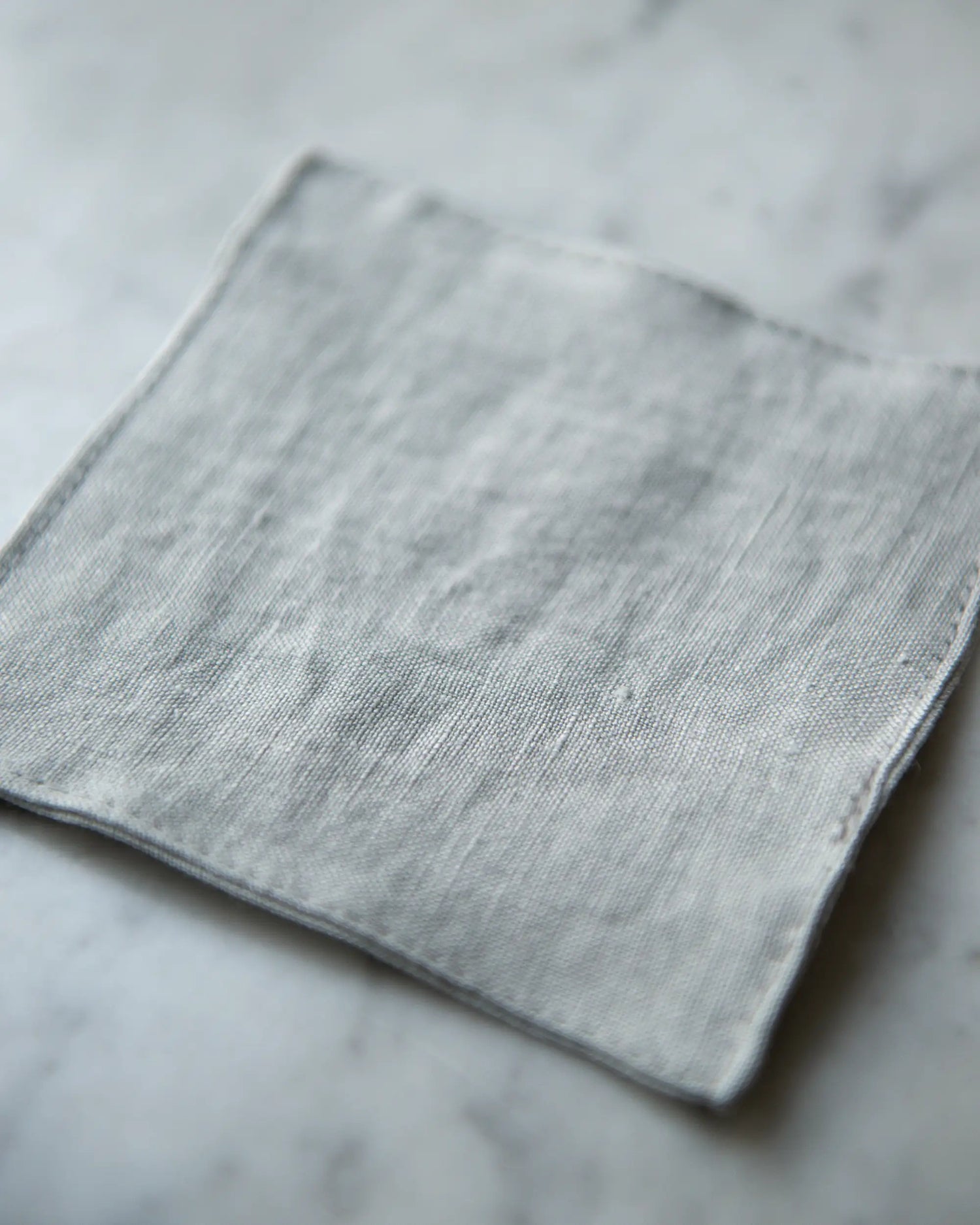 Ett grått handsytt glasunderlägg i linne. 