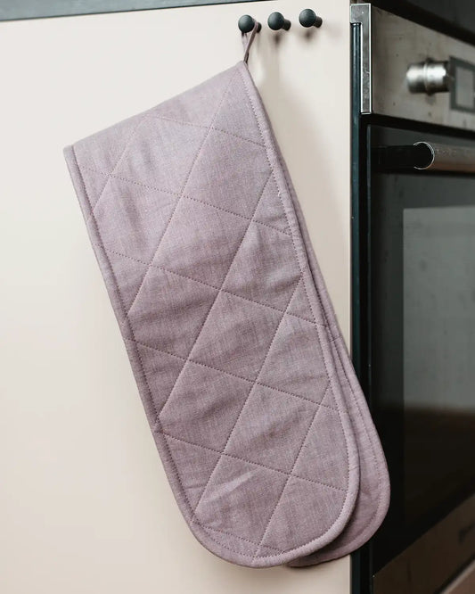 En ljusrosa dubbel grytvante i linne hänger i sin ögla på en krok.