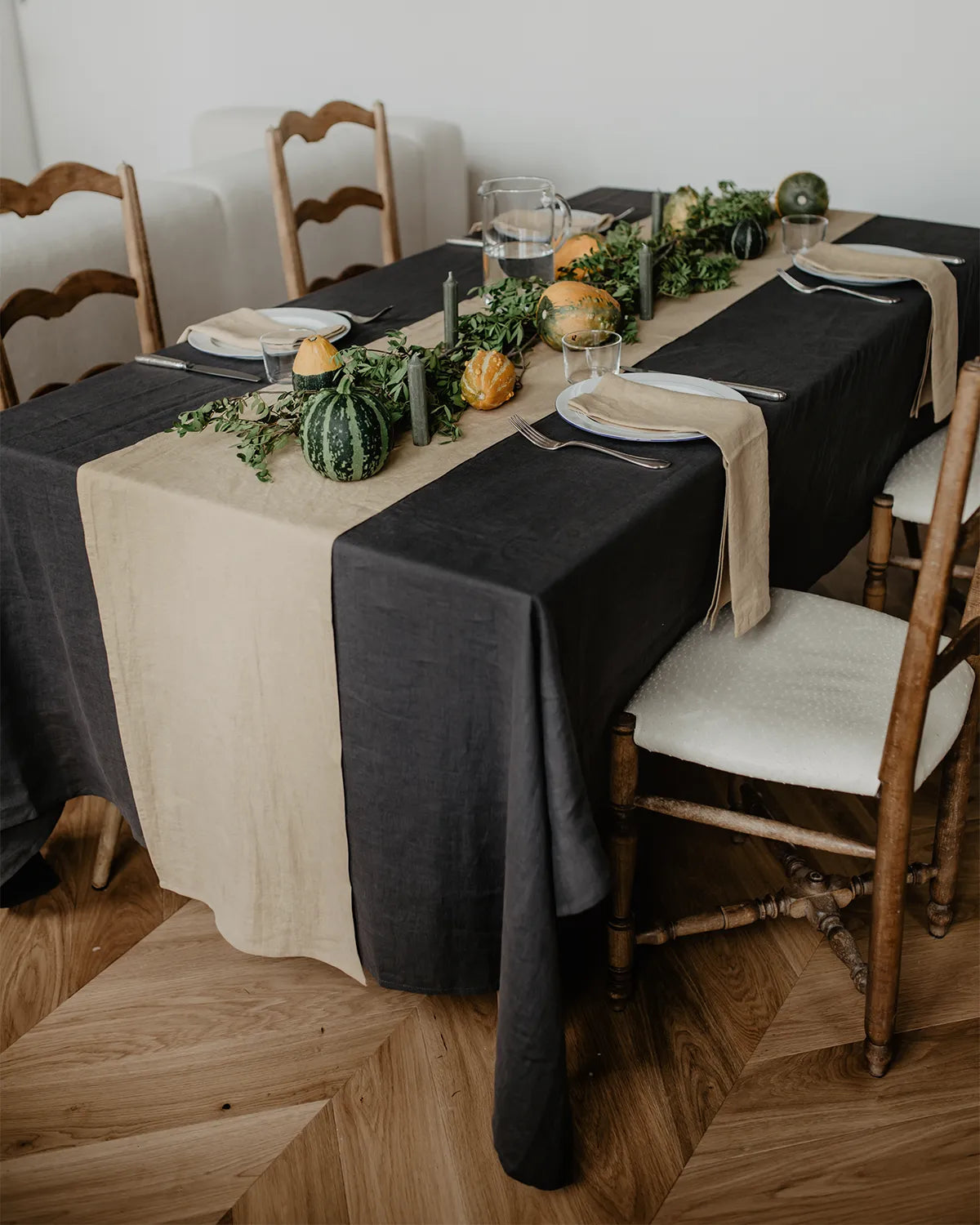 En rektangulär mörkgrå linneduk ligger på ett bord som är dukat till fyra personer. 