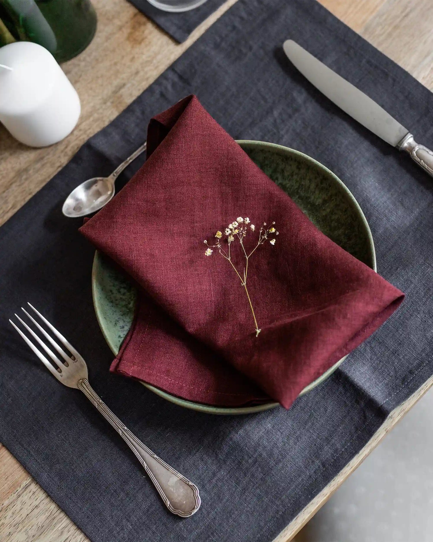 En röd tygservett i linne ligger på en tallrik tillsammans med en bordstablett i linne och silvriga bestick. 