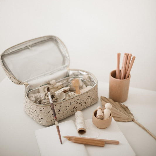 En stor rektangulär necessär i naturell linne står på ett bord öppen med målarinnehåll.