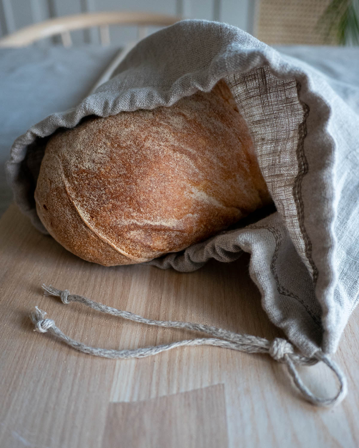 En brödpåse i naturell linne som ligger på ett bord med ett surdegsbröd som skymtar i öppningen. 