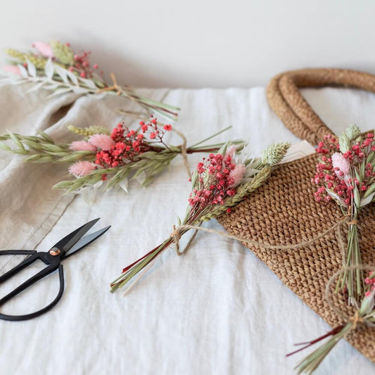 Små torkade buketter av blommer är fastknutna i en girlang och ligger på ett bord.