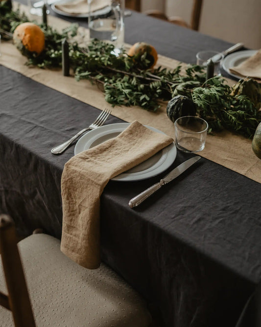 Ett dukat bord med textilier i mörkgrått och senapsgult tillsammans med bordsdekorationer av gröna blad och orangea pumpor.