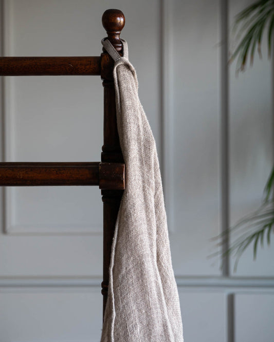 Handduk i naturell linne som hänger i en ögla på en stolskant. 