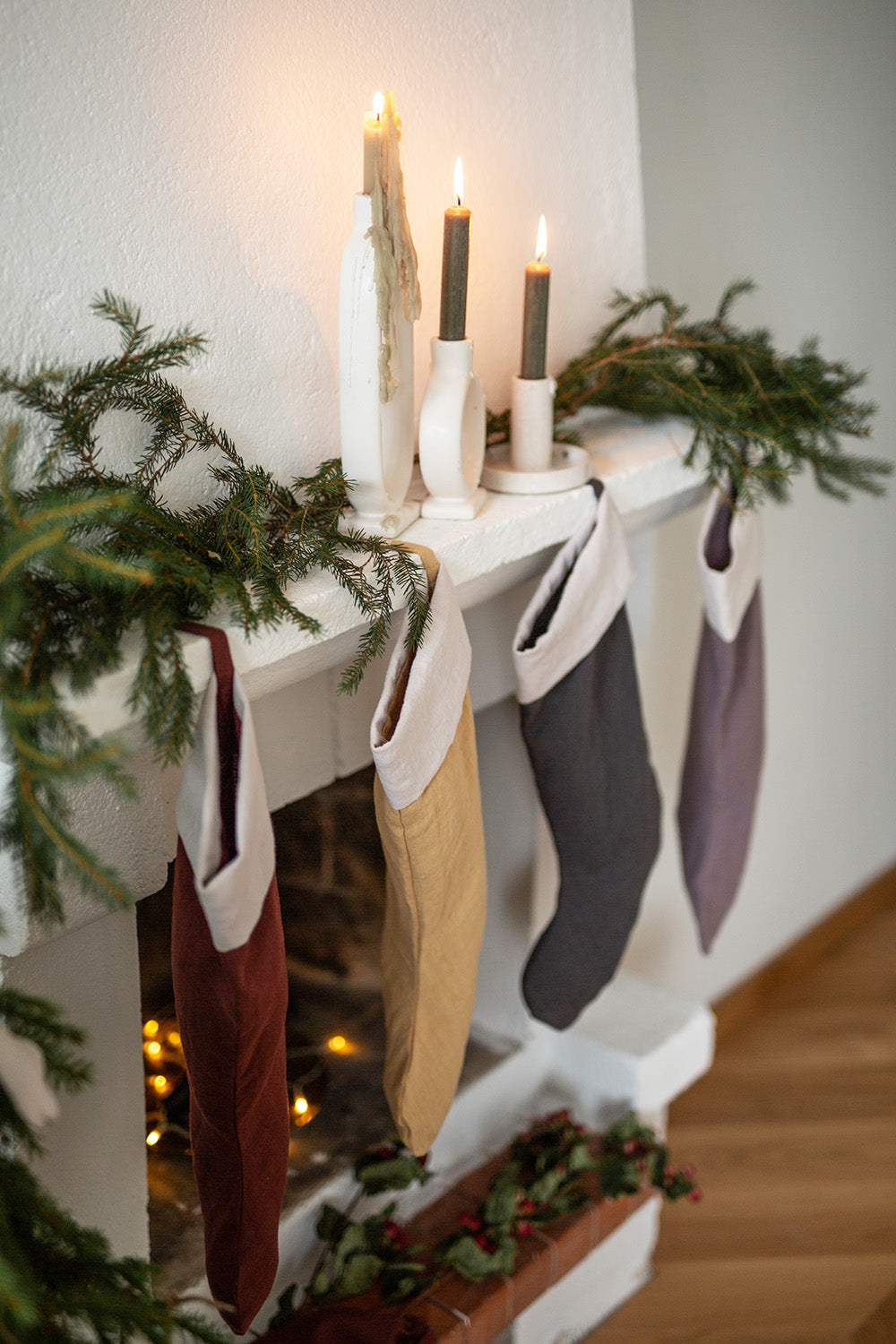 Flera julstrumpor i linne hänger framför en elstad i sina öglor. 