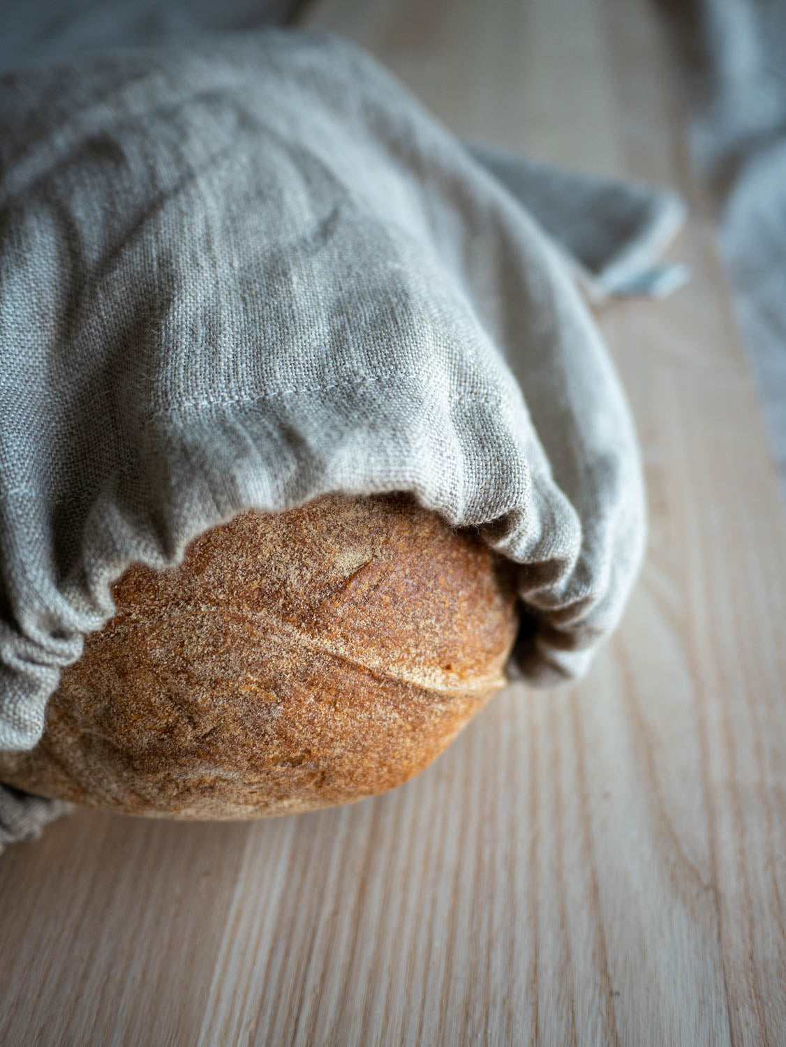 Brödpåse av naturell linnetyg där ett surdegsbröd skymtar i öppningen.