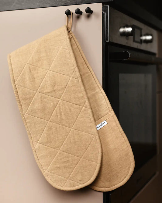 En stor beige dubbel grytvante i linne hänger i sin ögla på en svart krok