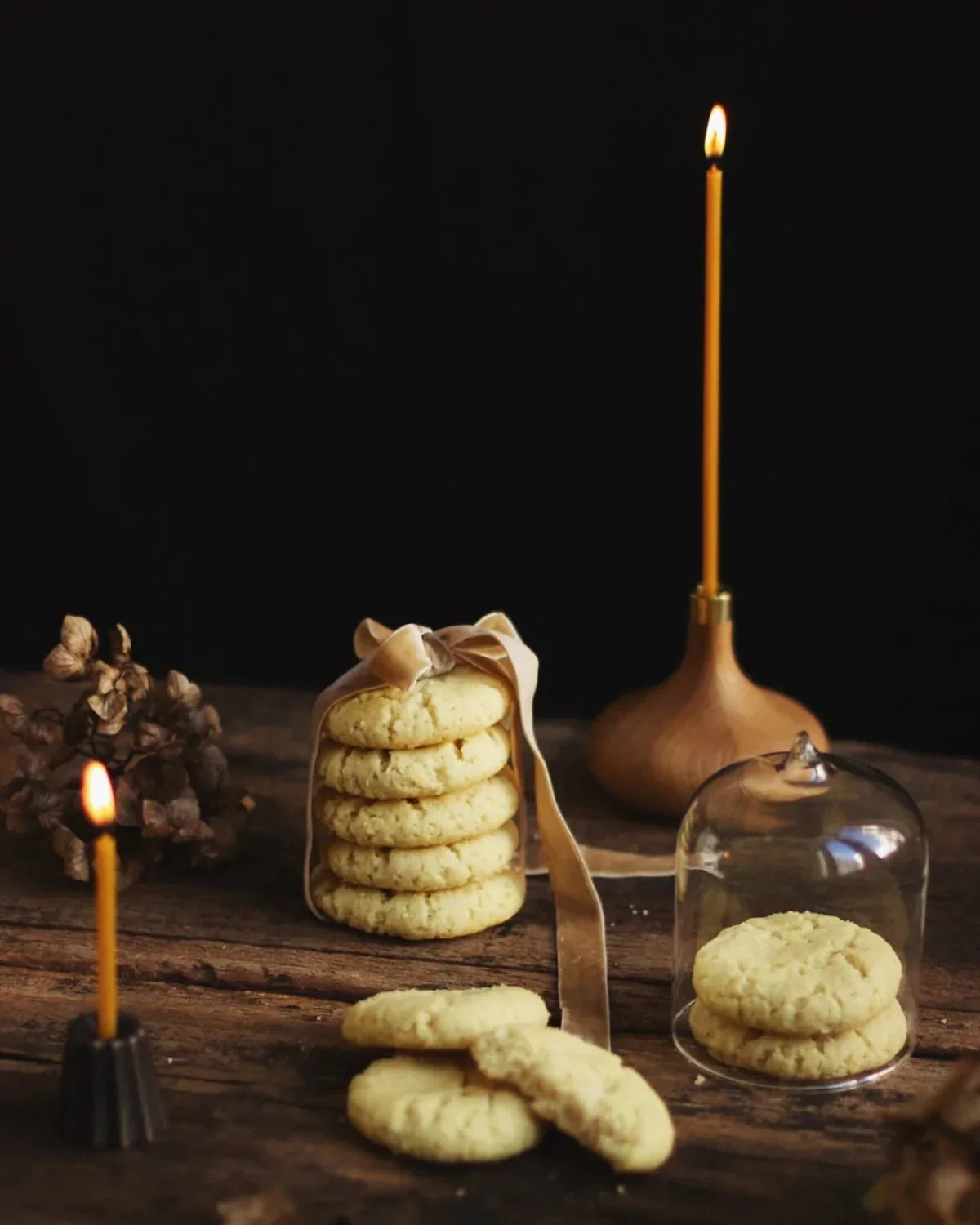 Handgjorda ljushållare i ek och brons och ljus i bivax står på ett bord med kakor. 