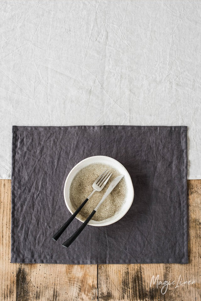 Rektangulär mörkgrå bordstablett i linne som ligger på ett rustikt träbord med en vit linneduk.