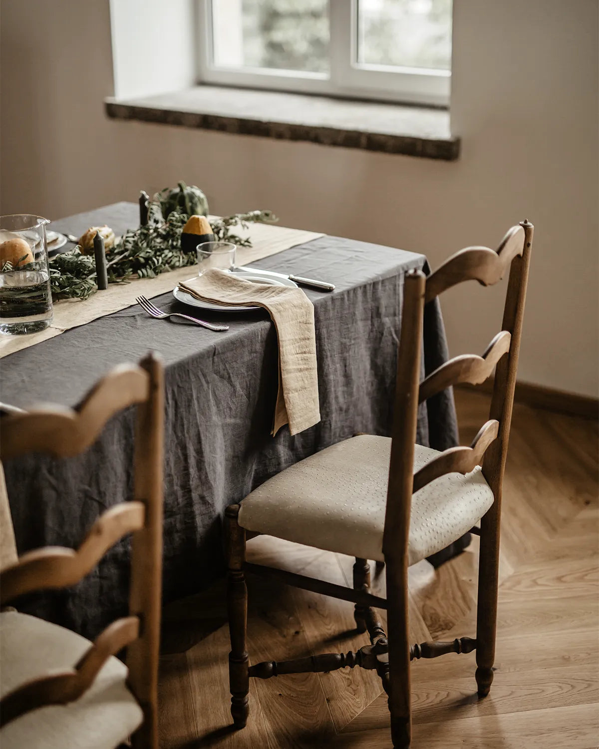 En rektangulär mörkgrå linneduk ligger på ett bord med andra linnetextiler.  